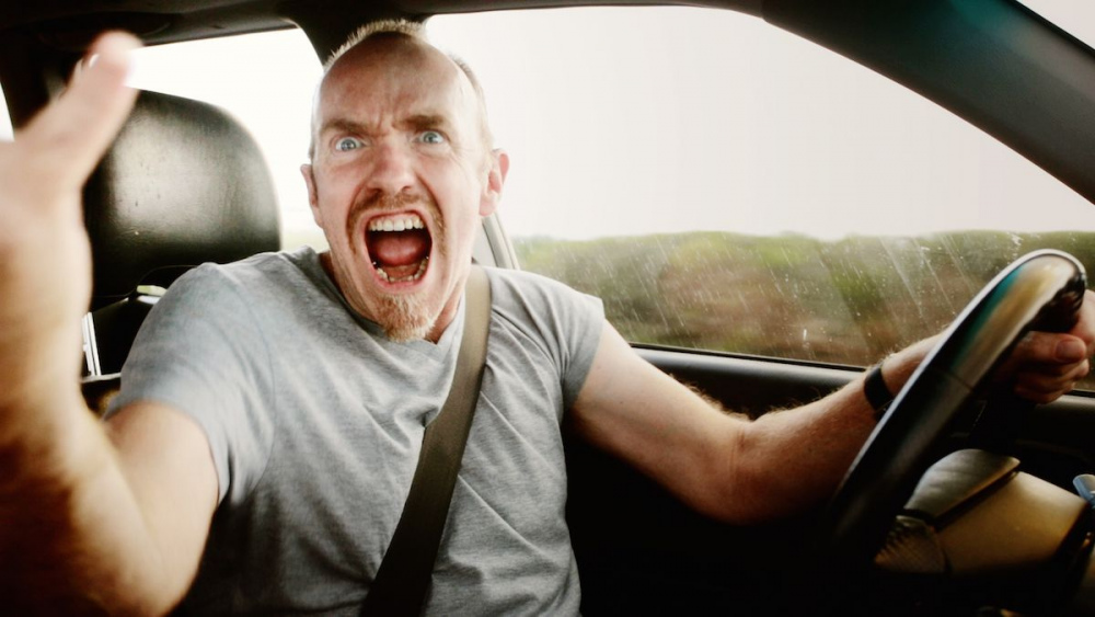 An-angry-man-glares-through-his-passenger-side-window-gesturing-and-yelling-in-a-fit-of-road-rage.jpg